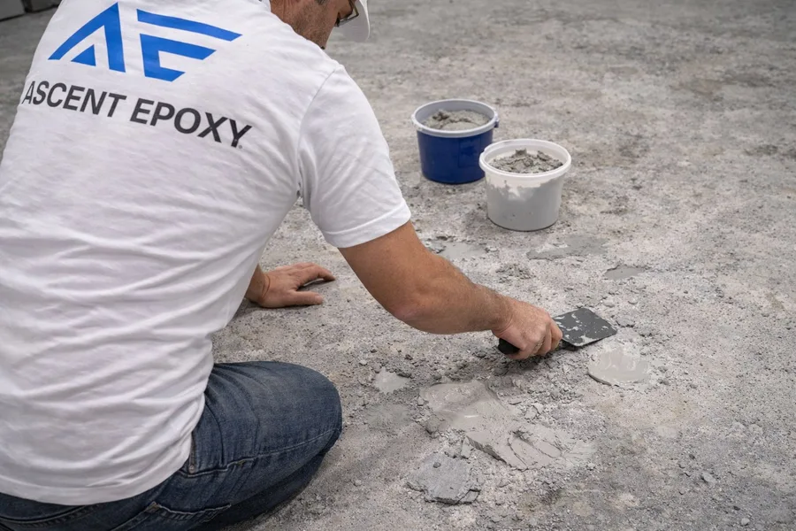 Ascent Epoxy technician applying epoxy filler compound to repair pitted concrete substrate with trowel before recoating