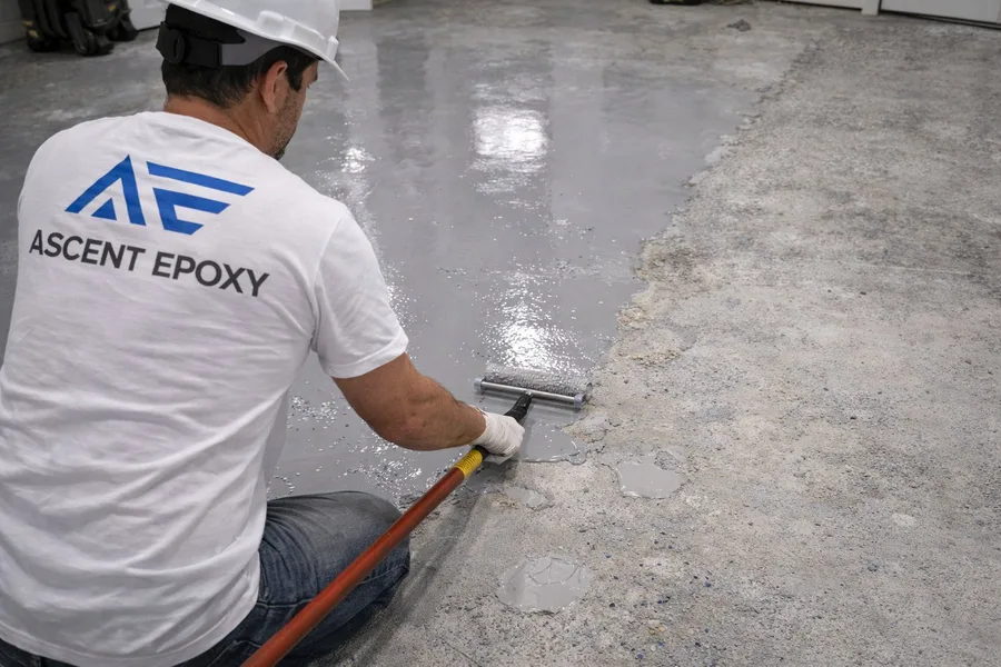 Ascent Epoxy installer applying fresh epoxy re-coat to repaired garage floor with roller, bridging old and new surface